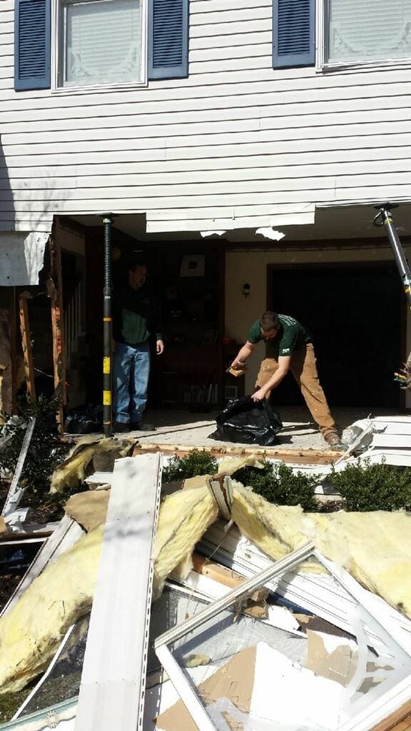 Workers clearing debris from a house damaged by vehicle impact