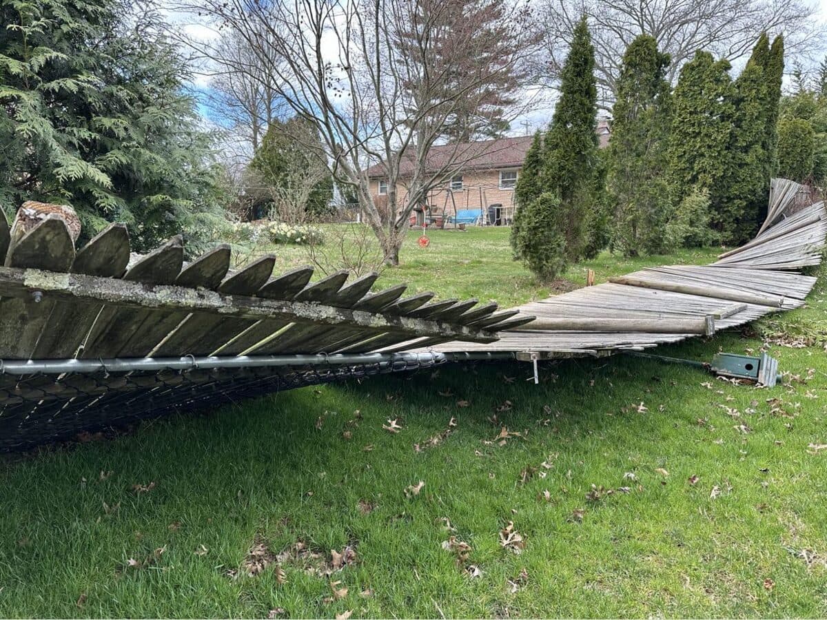 Wind-toppled wooden fence stretched across a backyard after a storm
