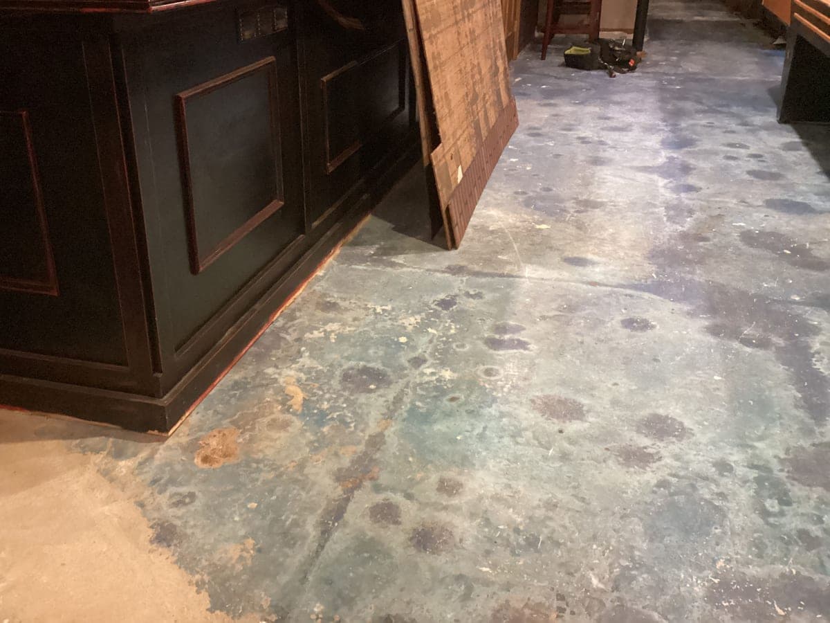 Basement bar with the flooring removed down to stained bare concrete — before